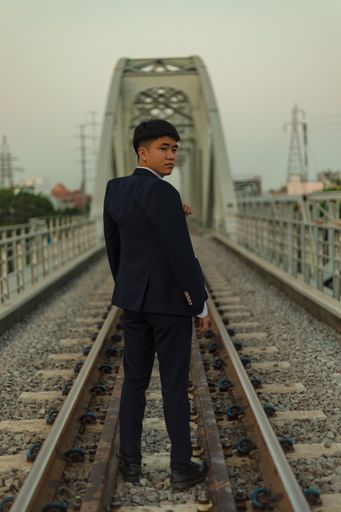 A confident young Asian man in a suit standing in the middle of a railway looking back