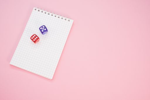 A top view of two rolling dices on a notebook isolated on a pink background