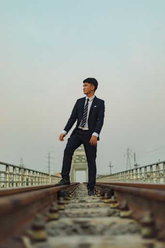 A low angle shot of a young Asian man in a suit staning in the middle of a railway while looking away