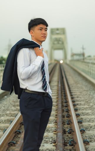 A young Asian businessman standing in the middle of a railway holding tuxedo coat over his shoulder