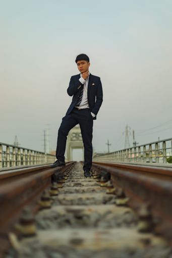 A young Asian businessman standing in the middle of a railway with his hand on his neck
