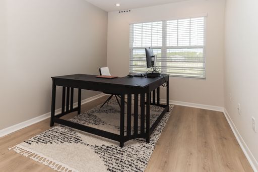 a pristinely clean, empty room with a desk situated in the corner, and natural light from the windows