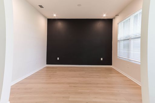 An empty and minimalist living space, with a black wall and hardwood floors
