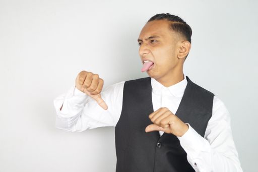 A portrait of a disgusted South Asian man showing the thumbs-down gesture against a white wall