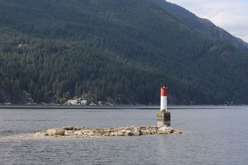 A scenic view of a lighthouse against green mountains of North Vancouver, Canada