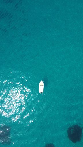 An aerial view of a boat in crystal clear blue ocean waters of Corfu Island in Greece.