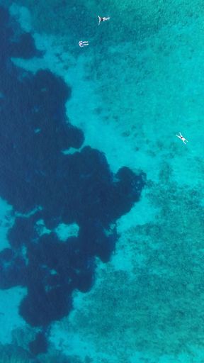 An aerial view of boats in crystal clear blue ocean waters of Corfu Island in Greece.
