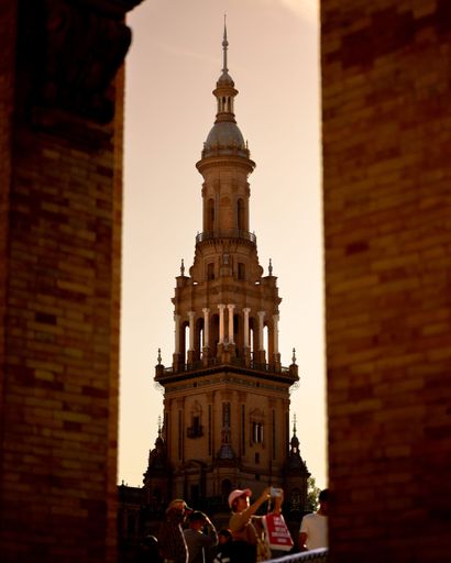 An aged clock tower is visible through a stone archway in Sevilla, Spain