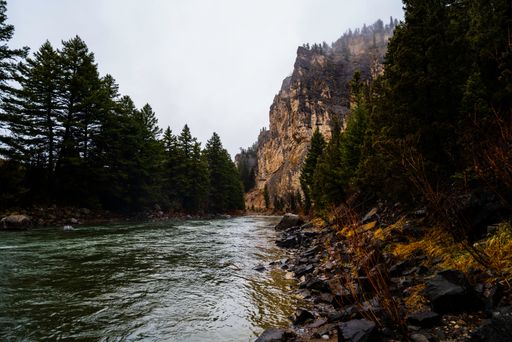 A landscape of a river surrounded by mountains on a gloomy day in Big Sky, Montana