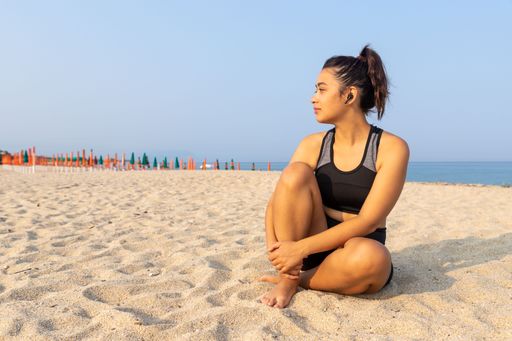 A young latina female in athleisure sitting on a beach