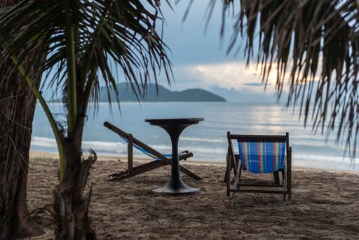 A wooden table and two folding chairs placed on the beach overlooking the calm sea