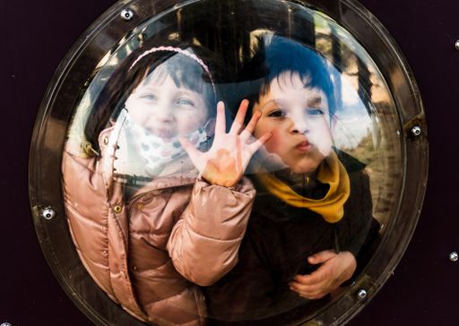 Young Polish Caucasian boy and girl behind a transparent window of a equipment doing crazy faces at a playground in the Malta park.