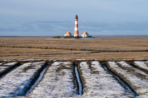 A lighthouse in a rural winter landscape seen through fields in Westerhever, North Sea, Germany