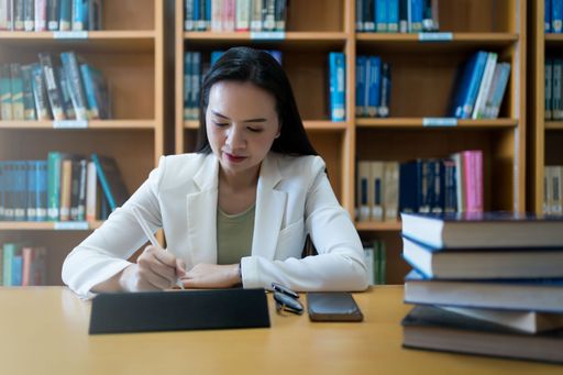 A Southeast Asian female lecturer sits at a small table, working at the library