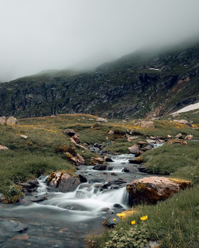 A picturesque scene of a small mountain stream meandering through a lush valley surrounded by snow-capped peaks