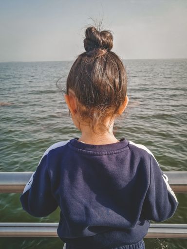 A small girl wearing sporty outfit, standing on the bridge and looking at the seascape