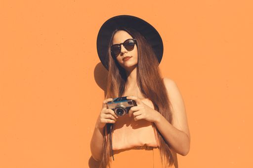 A Spainish woman with a vintage photo camera and wearing sunglasses isolated on an orange background