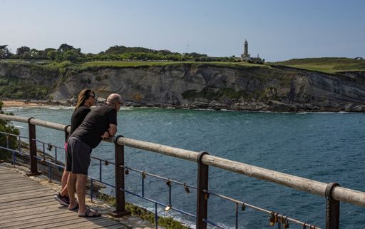 A couple standing at a scenic overlook, admiring the nearby lighthouse in Spain