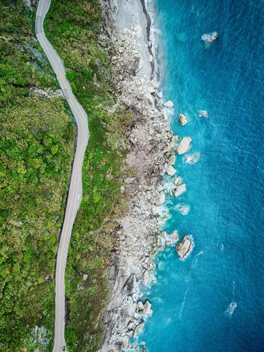 An aerial top view of a road along a green coastline against the sea waves