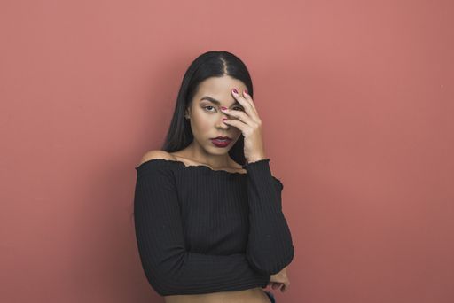 A beautiful shot of a sexy Hispanic woman covering half of her face on a pink background