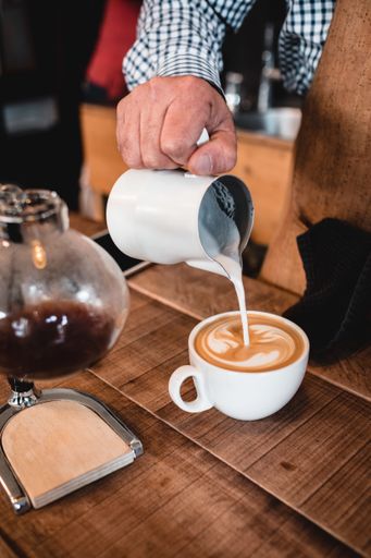 A vertical shot man pouring milk into cappuccino