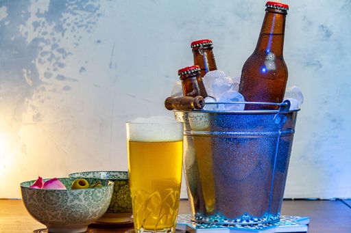 A selective focus shot of a glass of beer, snacks, and bottles of beer in a metal bucket with ice