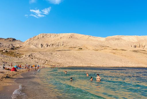 Tourists on beautiful beach surrounded by rocky hills. Rucica beach near Metajna on Pag island in Croatia.