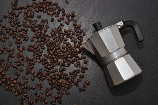 A top view of the aMoka pot on the black surface covered with scattered roasted coffee beans