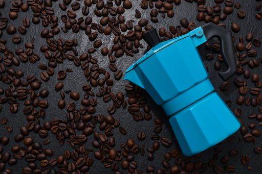 A top view of the Moka pot on the black surface covered with scattered roasted coffee beans