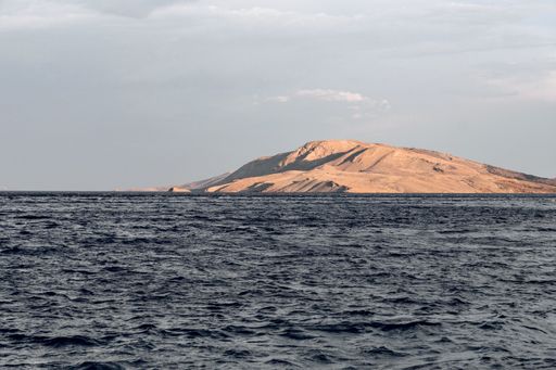 A closeup shot of a small island on the sea against cloudy sky background