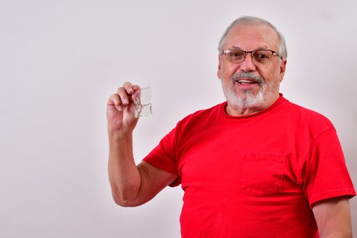 A senior male in a red shirt holding a bag of disinfectant in front of a white wall