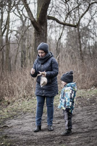 Unidentified woman holding a bag with bread next to a toddler boy in a forest on a cold winter day