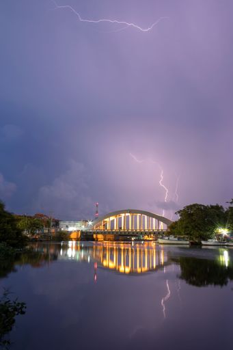 A vertical shot of lightning striking over the illuminated Bridge of the Plaza Rio San Juan