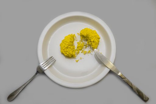 A top view of a yellow marigold on a plate with a fork and a knife on the gray surface
