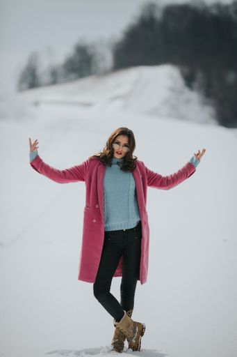 A vertical shot of a stylish Bosnian woman posing near the snowy forest in the winter