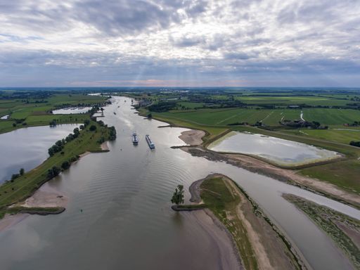 A high angle shot of typical dutch landscape with transport ship vessels in a river lek with a cloudy sky in the background