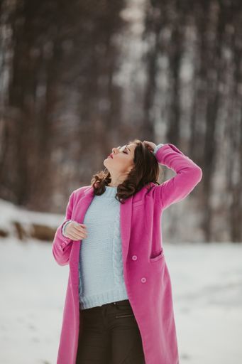 A vertical shot of a stylish Bosnian woman posing near the snowy forest in the winter