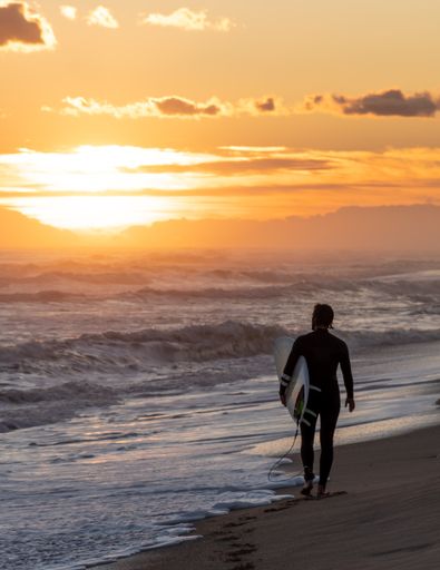 A vertical shot of a surfer running on the beach at golden sunset