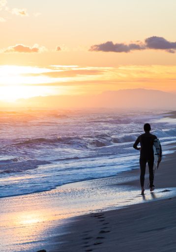 A surfer on the beach running during the golden sunset
