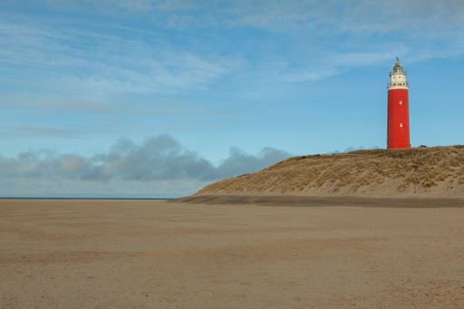 A wide shot of a red lighthouse in dunes of texel national park in netherlands