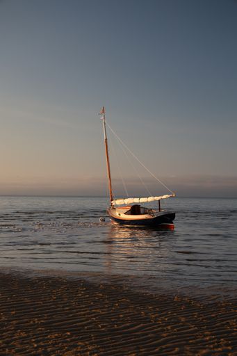 A vertical shot of the sandy beach and a sailboat in the blue sea during sunrise