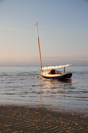 A vertical shot of the sandy beach and a sailboat in the blue sea during sunrise