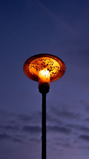 A vertical low angle shot of a glowing old street lamp under a blue sky