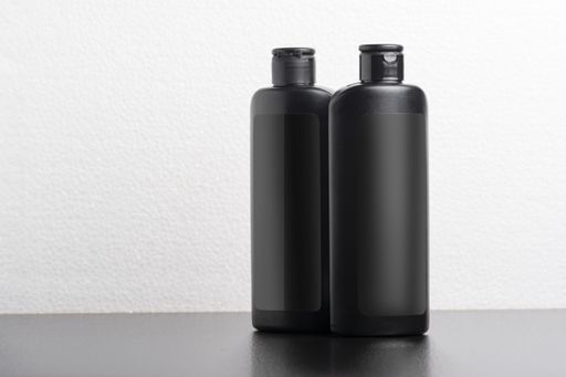 A selective focus shot of black shampoo bottles on a gray table on a white background