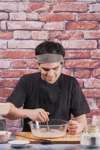 A vertical shot of a young Hispanic male baker mixing ingredients in a bowl to prepare bread dough