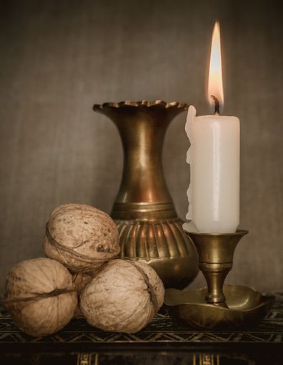 A vertical shot of a composition of a burning candle with walnuts and an old vase against a brown background