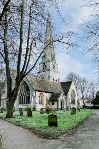 Church on a green lawn surrounded by graves, and trees. Two paths past the church
