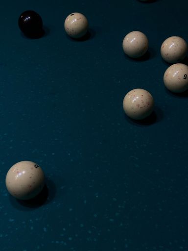 A vertical shot of white and black  billiard balls on a green  billiard table  under the light