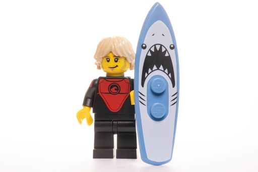 A yellow LEGO minifigure with a shark-faced surfboard on a white background