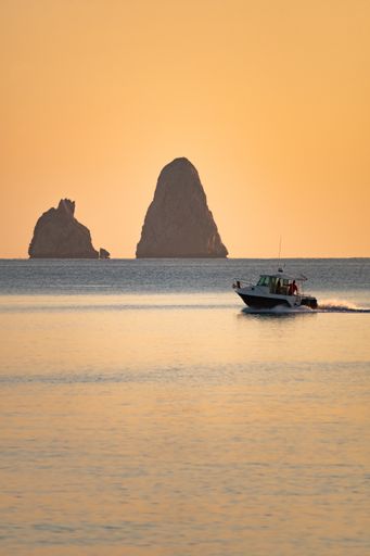 A vertical shot of people on sailing boat at dawn with islands on the background